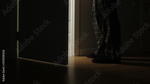 Adult man in a pajamas walks to a bathroom in the night