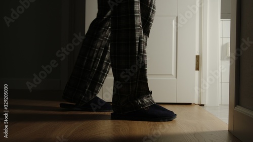 Aged man in a pajamas and slippers walks to a toilet at home in the night