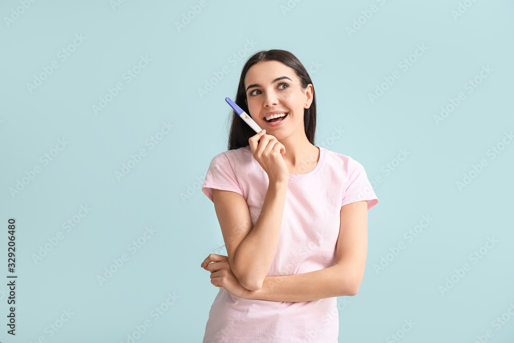 Happy young woman with pregnancy test on color background Happy young woman with pregnancy test on color background