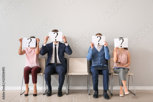 Young people holding paper sheets with question marks while sitting on chairs indoors. Job interview concept