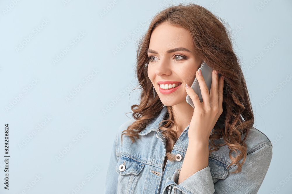 Fototapeta premium Young woman talking by mobile phone on color background