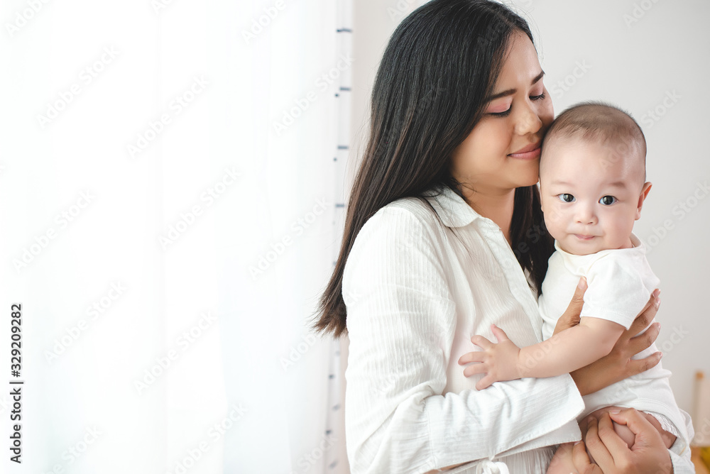 Asian mother holding his child happily. In the bedroom with white curtains. Motherhood, family relationship, new born baby, love of mother to her son or daughter concept. Asian mother holding his child happily. In the bedroom with white curtains. Motherhood, family relationship, new born baby, love of mother to her son or daughter concept.