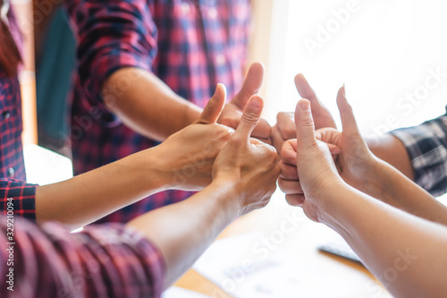 top view of employees standing around in a circle with their thumbs up and fists against each other, representing teamwork, positivity, community, help and support within small businesses or company..