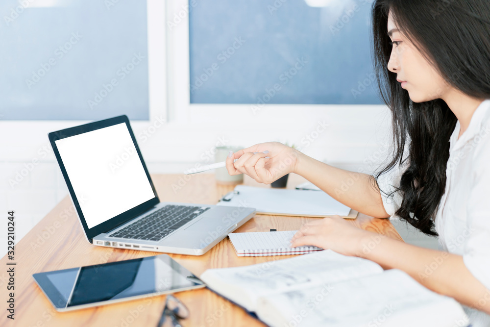 Fototapeta premium Education study abroad, Overseas Asian student girl sitting at table looking book while do homework by laptop making video call abroad to internet friend connection, happy mood smile broadly library