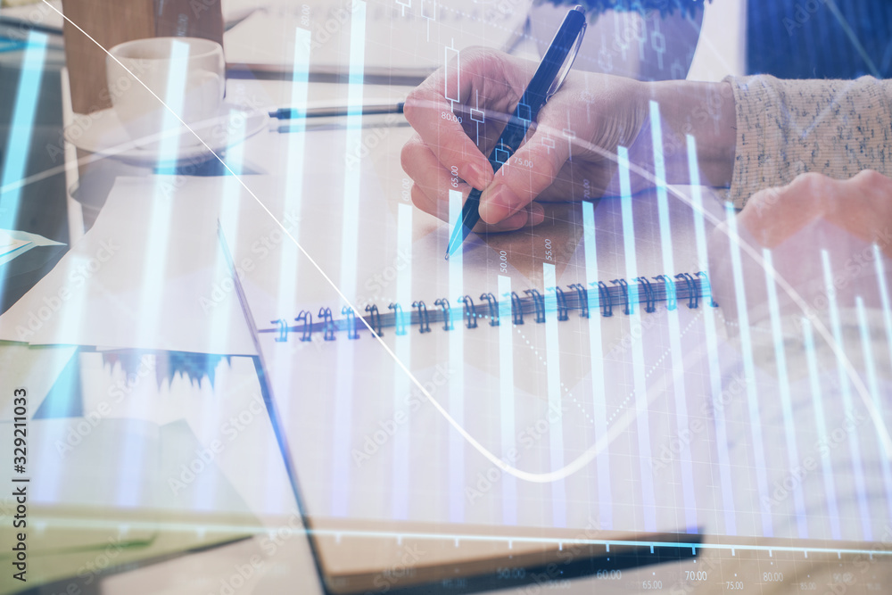 Hand taking notes in notepad. Forex chart holograms in front. Concept of research. Double exposure
