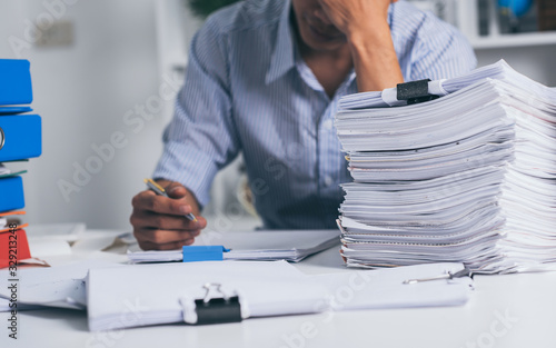 Young asian exhausted businesssman with messy desk and stack of papers, working busy, overwork. photo