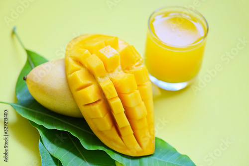 Mango summer juice in glass with sweet ripe slice of mango on green leaves from tree tropical fruit