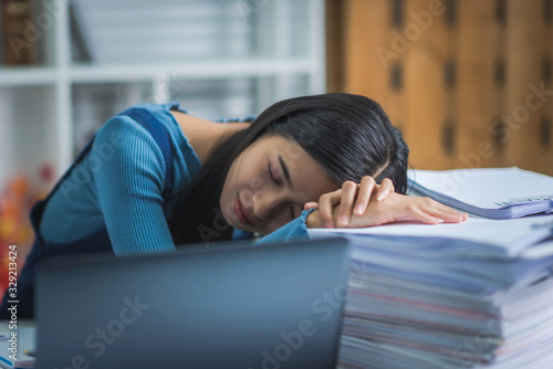 Young business female sleeping at desk table, tried attrative woman with stack of papers. photo