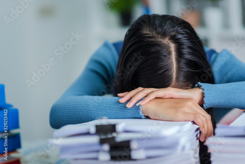 Young business female sleeping at desk table, tried attrative woman with stack of papers. photo