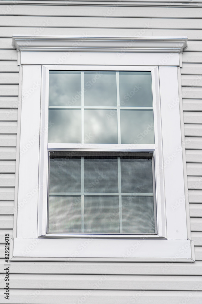 Stand alone double hung window with fixed top sash and bottom sash that slides up, sash divided by two white grilles, surrounded by thick white elegant frame and decorative trim on a new residence Stand alone double hung window with fixed top sash and bottom sash that slides up, sash divided by two white grilles, surrounded by thick white elegant frame and decorative trim on a new residence