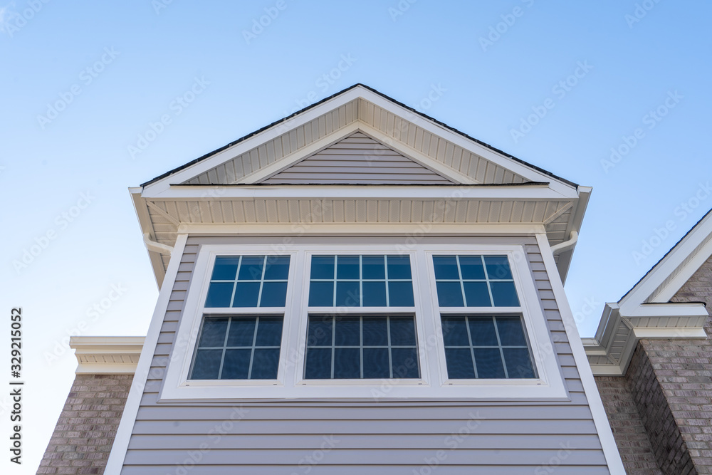 Double hung window with fixed top sash and bottom sash that slides up, sash divided by white grilles a surrounded by white elegant frame on a horizontal vinyl siding, under a gable and soffit