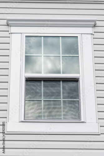 Stand alone double hung window with fixed top sash and bottom sash that slides up  sash divided by two white grilles  surrounded by thick white elegant frame and decorative trim on a new residence