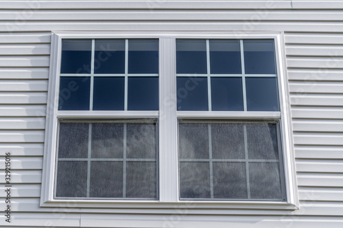 Double hung window with fixed top sash and bottom sash that slides up, sash divided by two white grilles, surrounded by white elegant frame horizontal white vinyl siding on new residence
