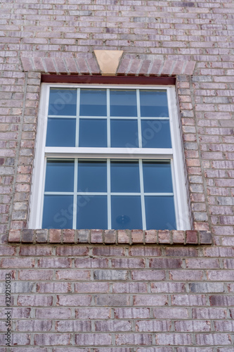 Stand alone double hung window with fixed top sash and bottom sash that slides up, sash divided by three white grilles, surrounded by brick lintel and frame, decorative trim on a new residence