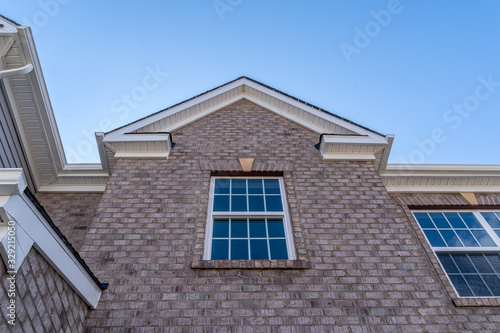 Stand alone double hung window with fixed top sash and bottom sash that slides up, sash divided by three white grilles, brick frame and facade siding, gable with fascia
