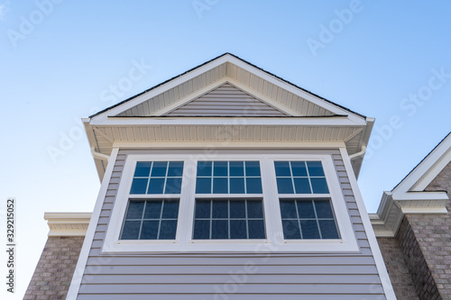 Obraz na płótnie Double hung window with fixed top sash and bottom sash that slides up, sash divided by white grilles a surrounded by white elegant frame on a horizontal vinyl siding, under a gable and soffit w salonie