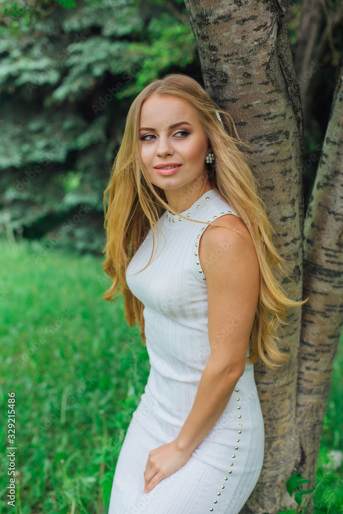 Portrait of a charming blond woman wearing beautiful white dress standing next to rowan tree. Portrait of a charming blond woman wearing beautiful white dress standing next to rowan tree.