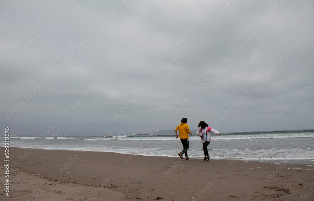 cute and young couple runnings from the water, sea, ocean, waves on the beach