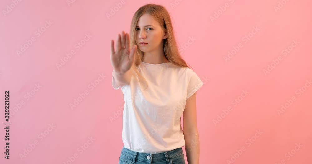 A young serious girl in a white t-shirt shows a forbidding gesture on a pink background A young serious girl in a white t-shirt shows a forbidding gesture on a pink background