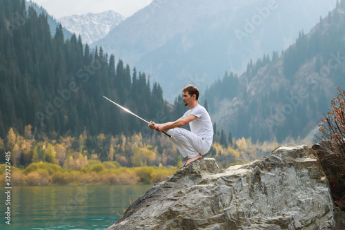 A barefoot man sits on a stone and holds a sword in his hands. Preparing for the battle. Man health concept photo