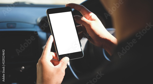 Cropped shot view The driver uses the phone while driving. Modern smart phone with round edges. Isolated screen for mockup. Car navigation display in background. 