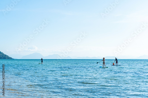 People on sup boards swim across the ocean near the beach
