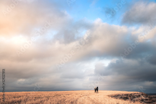 two adventurers walking in amazing endless fields with beautiful blue sky and lovely white clouds above their head and enjoying the freedom and peace.