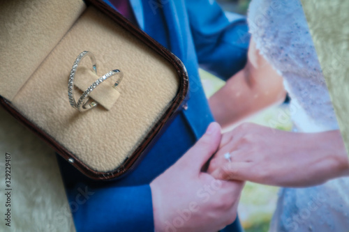 couple rings placed in the box. There is a photo of the groom holding the bride's hand Both lay on a white soft wool rug.