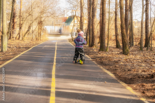 a child races on a scooter along an asphalt road in a spring park