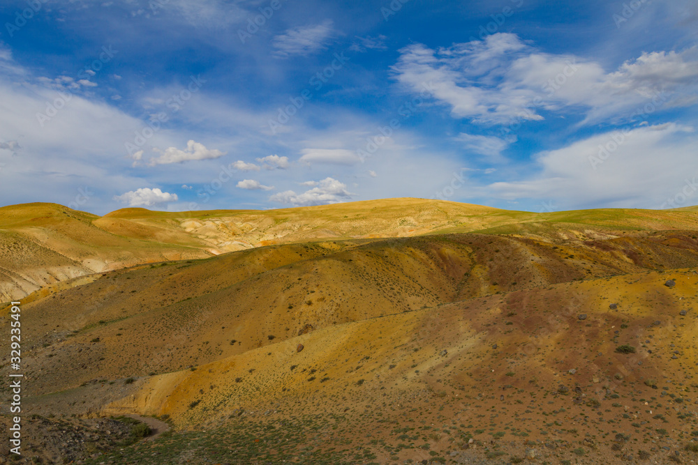 Panoramic view of a yellow sand mountain in Altai. Soft light, white clouds, blue sky.