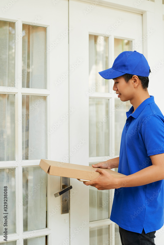 Delivery man in blue uniform bringing package to entrance doors of customer Delivery man in blue uniform bringing package to entrance doors of customer