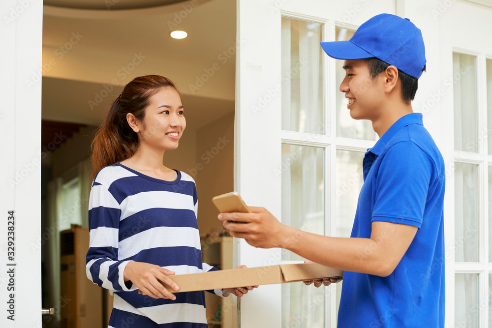 Fototapeta premium Cheerful courier giving pizza to young woman who ordered it online