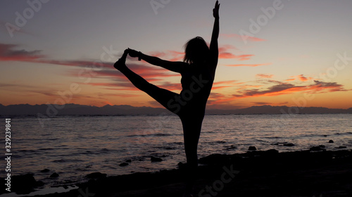 Silhouette of woman doing yoga extended hand-to-big-toe pose on sea sunset.
