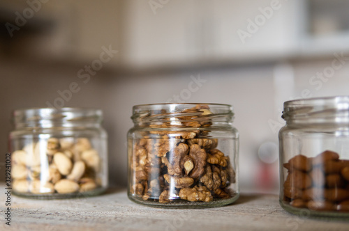 Almond, walnut and pistachio in a jars which standing on a white vintage table with a kitchen on background. Nuts is a healthy vegetarian protein and nutritious food. Nuts on rustic old wood.