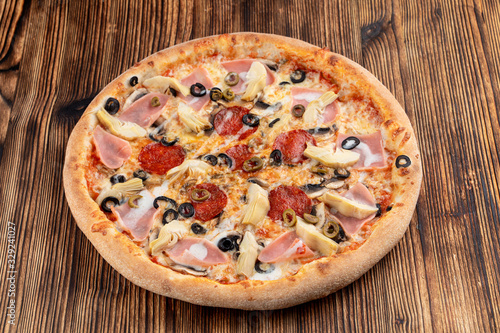 Pizza with artichokes and pepperoni on wooden table in italian restaurant