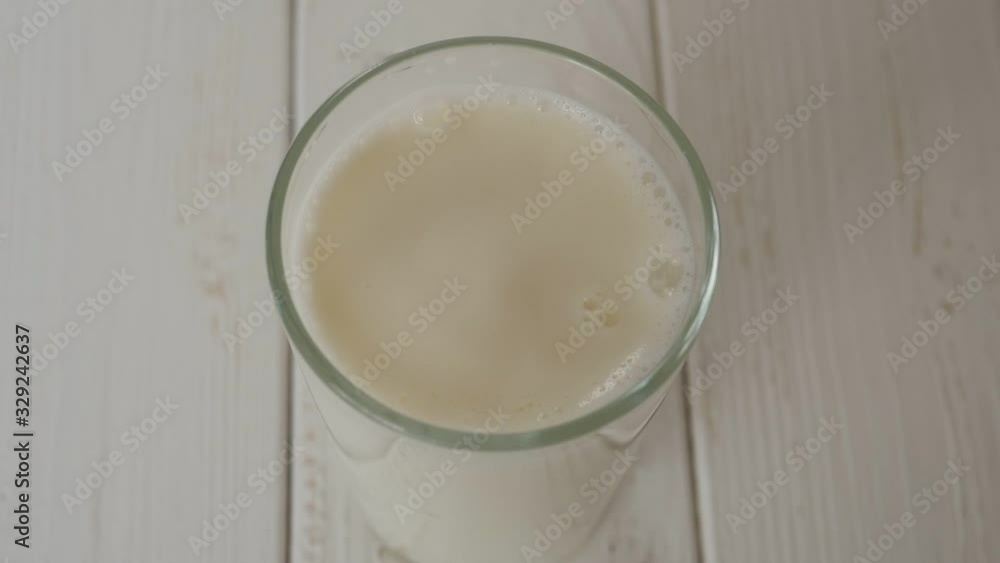 Close-up of milk drops falling into a full glass of milk on a light wooden surface, slow motion. The view from the top. Close-up of milk drops falling into a full glass of milk on a light wooden surface, slow motion. The view from the top.