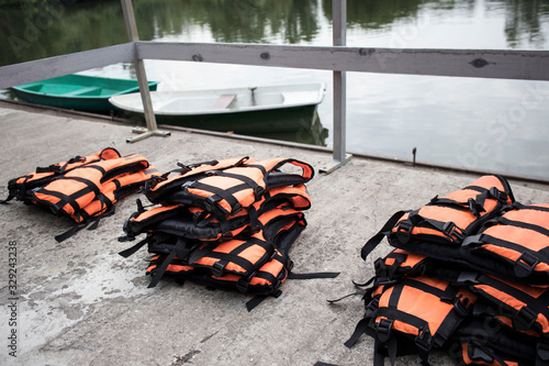 orange life jackets lie on the waterfront on the lake shore against the background of boats © Igorzvencom