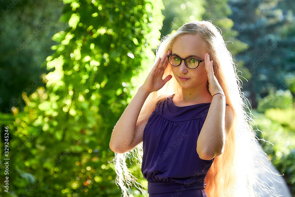 Pretty teenage girl 14-16 year old with curly long blonde hair in beautiful adult dress in the green park in a summer day outdoors. Beautiful portrait
