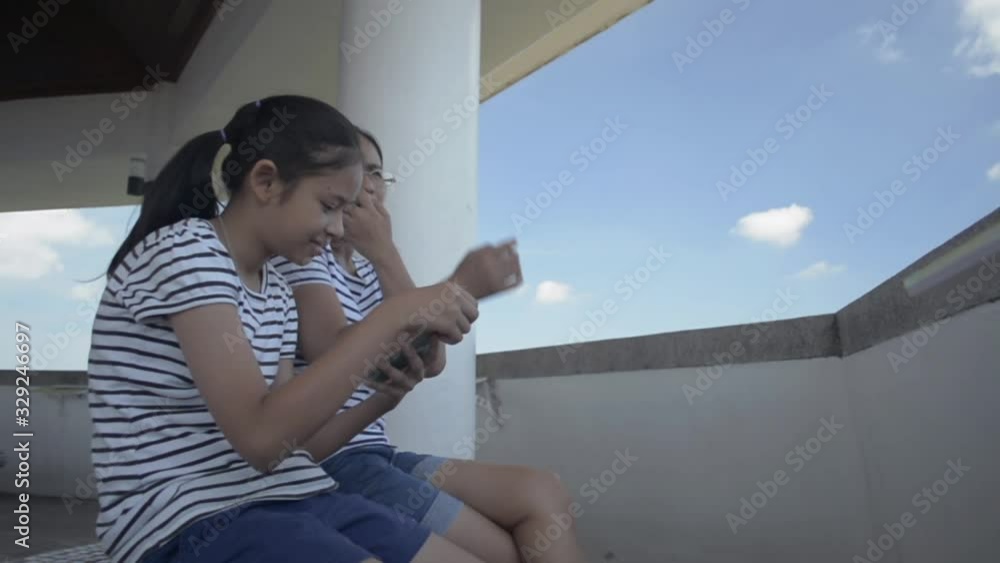 Mother and her daughter sitting and using mobile phone together while texting and chatting on social online at view point tower with blue sky. Mother and her daughter sitting and using mobile phone together while texting and chatting on social online at view point tower with blue sky.