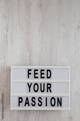 'Feed your passion' words on a lightbox on a white wooden background, top view. Overhead, from above, flat lay. Space for text.