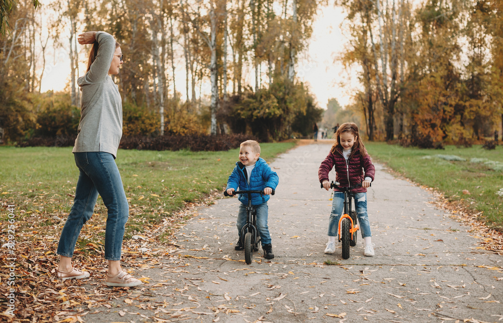 Fototapeta premium Caucasian mother giving the start for her kids who are riding the bikes in a sunny autumn day