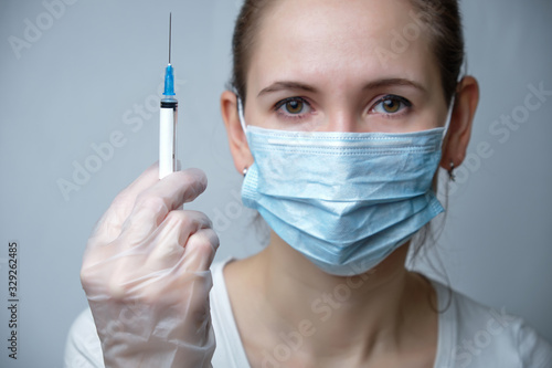 A nurse in a protective mask and gloves holds a syringe with copy space.