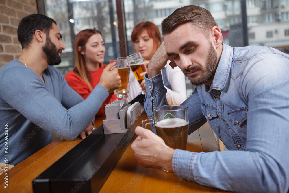 Young drunk man sleeping after drinking too much beer, his friends on background. Handsome man asleep at beer pub during meeting with friends Young drunk man sleeping after drinking too much beer, his friends on background. Handsome man asleep at beer pub during meeting with friends