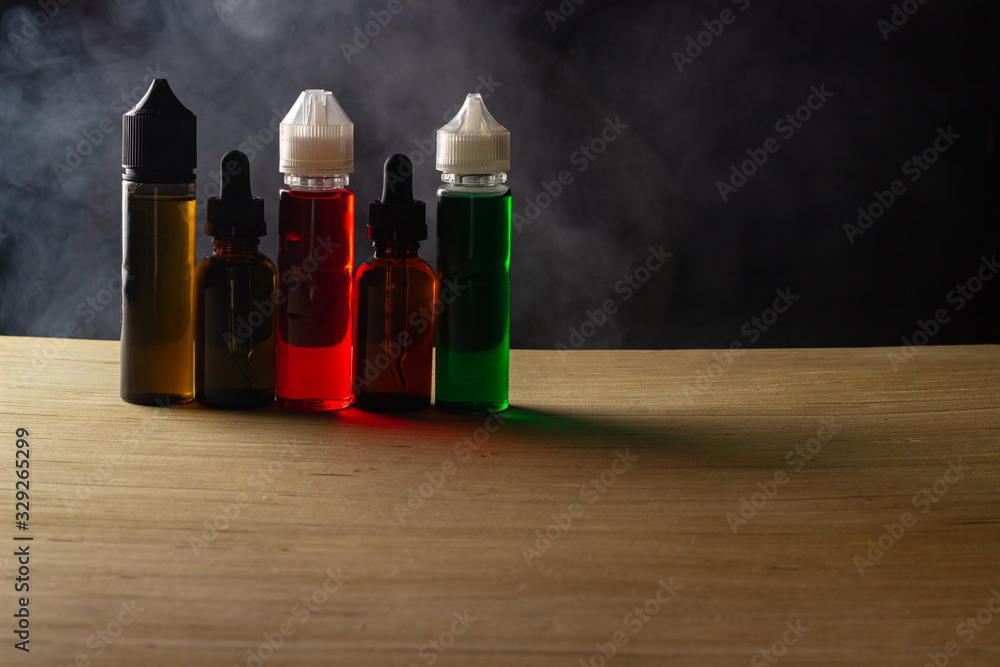 Gorilla bottles and liquid droppers for vaping on a wooden table in front of black background with clouds of steam Gorilla bottles and liquid droppers for vaping on a wooden table in front of black background with clouds of steam