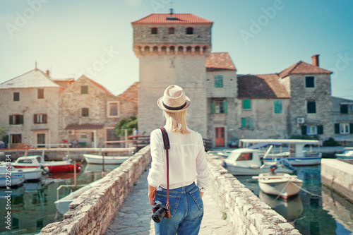 Photography and travel. Young woman walking with her camera near Kastel Gomilica Castle on Dalmatia coast, Croatia.