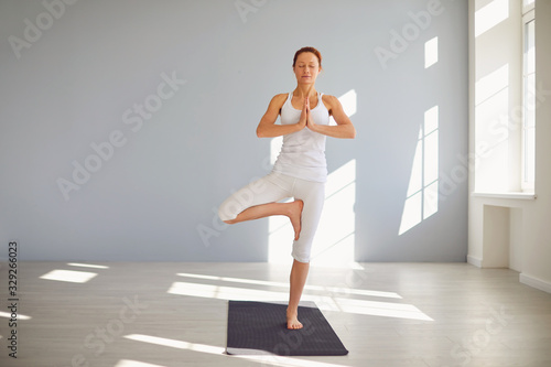 Yoga girl. Fitness woman in white sportswear standing in a yoga pose meditates relaxes sitting on the floor in a white classroom.