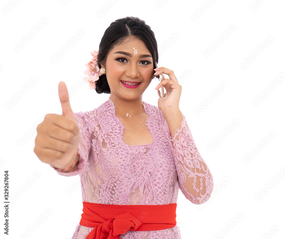 Young Balinese woman wearing traditional clothes when calling use smartphone with hands thumbs up Young Balinese woman wearing traditional clothes when calling use smartphone with hands thumbs up