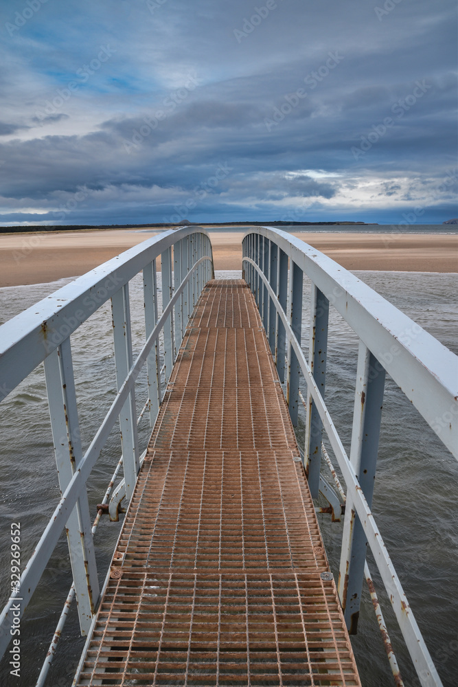 Fototapeta premium Publiczna kładka przy plaży Belhaven w Szkocji. Odetnij podczas przypływu. Koncepcja most donikąd, nieznane, podróż, przygoda.