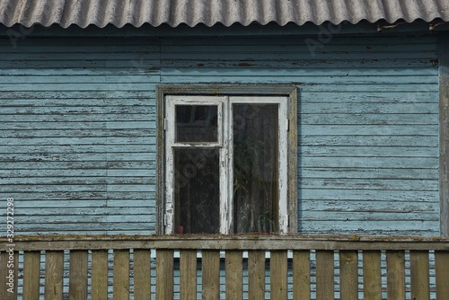 one white old window on a blue wooden wall of a rural house behind a green fence