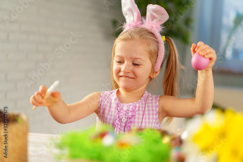 Toddler girl with bunny ears coloring eggs for Easter